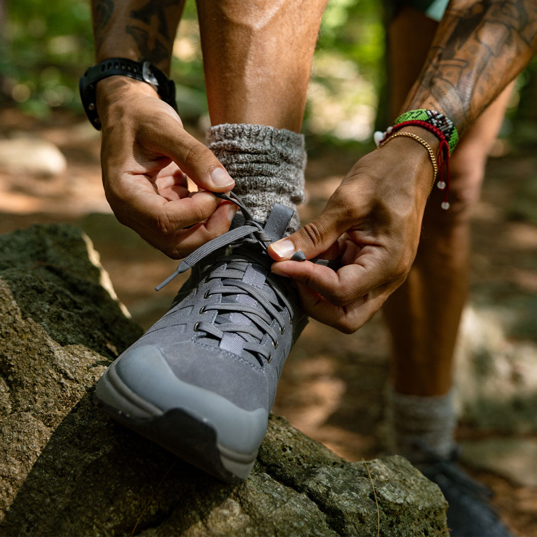 Person tying a gray hiking shoe outdoors on a rock