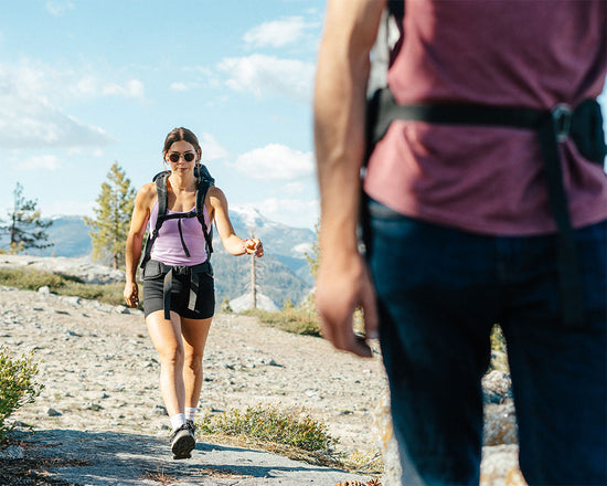 Two people hiking on a trail with mountains in the background