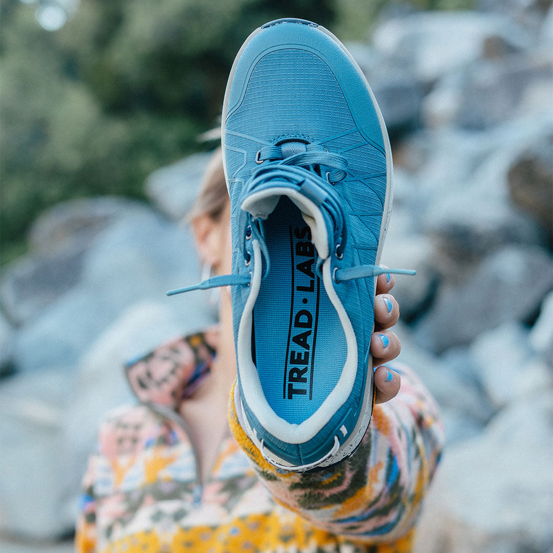 Person holding a blue sneaker with 'Tread Lab' branding against a blurred natural background