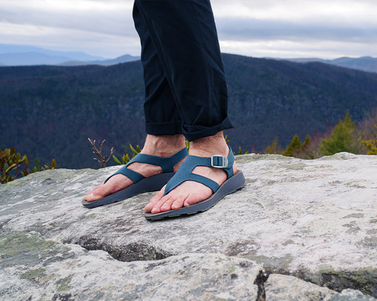 Man wearing blue Albion Sandals on the rocky peak at the top of a mountain in North Carolina